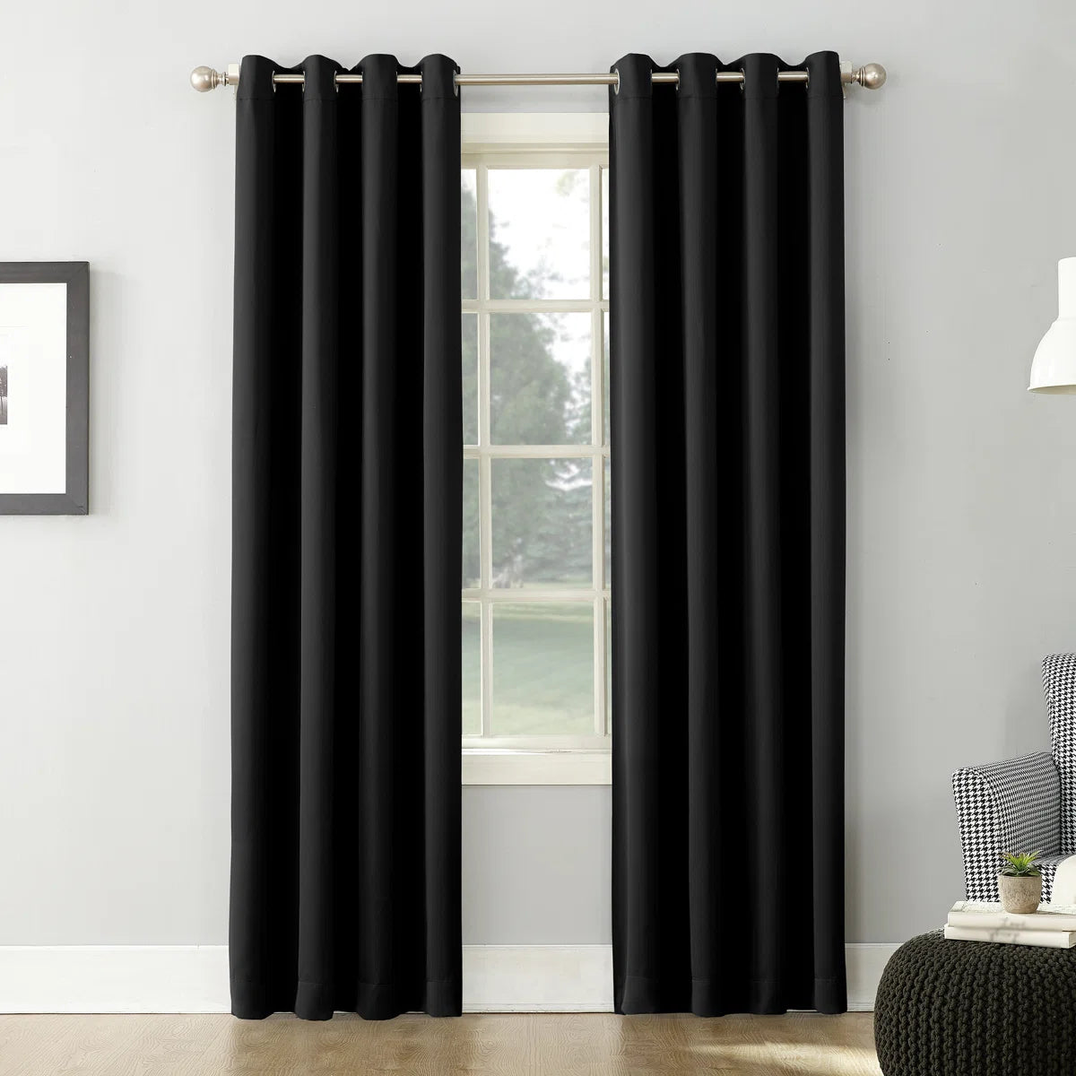 Black curtains hanging in front of a window with a neutral-colored wall and furniture in the background.