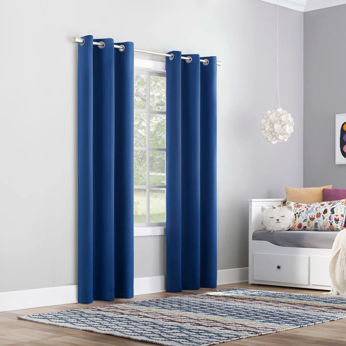 Blue curtains in a room with a window, rug, and small table with pillows.