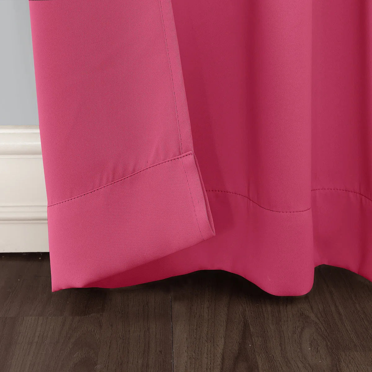 Close-up of a bright pink curtain on a wooden floor with a neutral wall background.