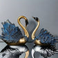 Two decorative swan figures with blue and gold feathers on a reflective surface.