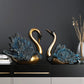 Two decorative swan figures on a dark surface with a plain background