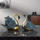 Two decorative swan statues on a marble surface with a neutral background