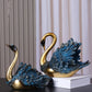 Decorative swan statues with gold and blue feathers on a dark surface.
