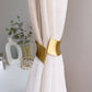 White curtain with gold tieback against a neutral background
