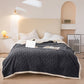 Gray textured blanket on a bed in a bedroom setting with a lamp and nightstand.