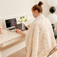 Woman in a white robe using a tablet at a desk with a laptop and plant.