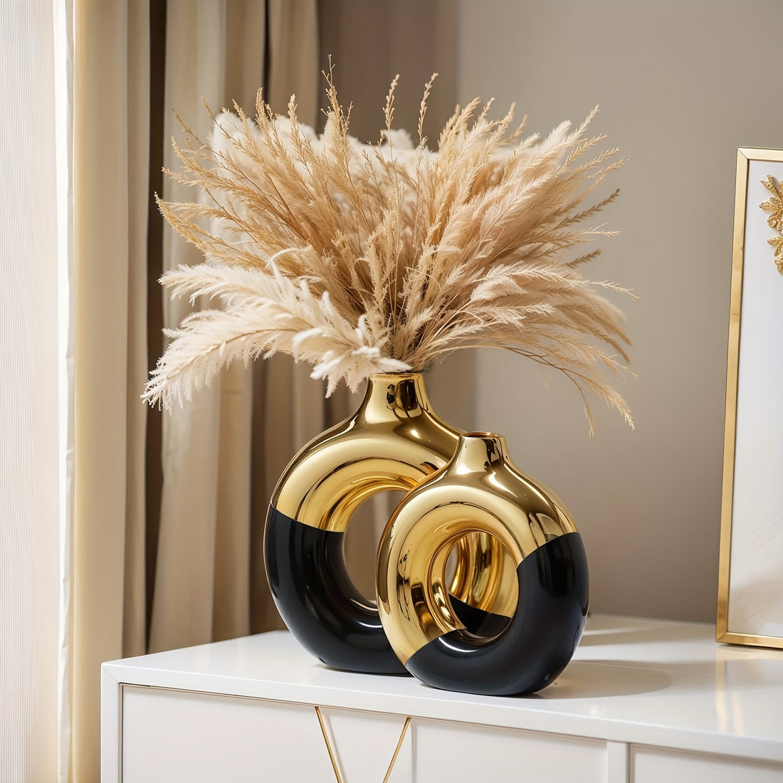 Decorative vase with gold and black design on a white surface, featuring dried pampas grass.