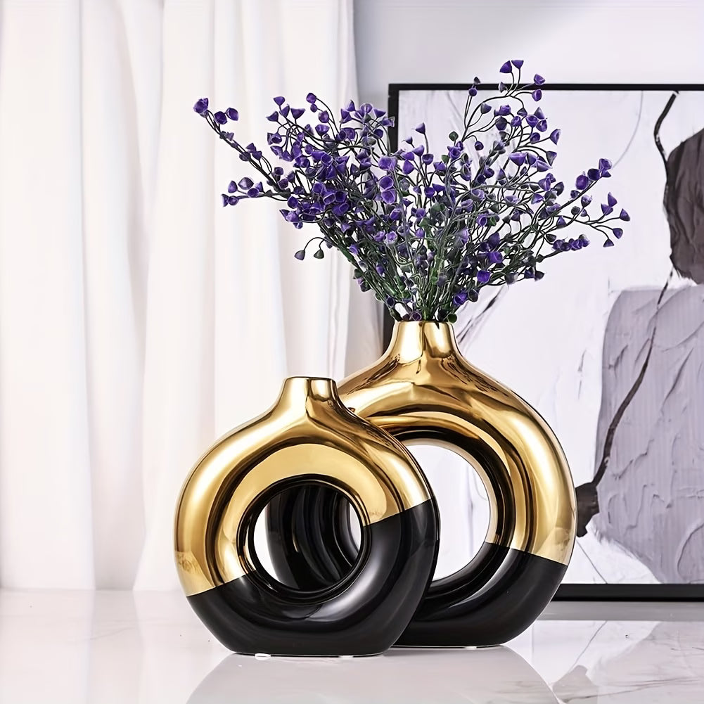Two gold and black vases with purple flowers on a white surface.