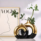 Two black and gold vases with a plant against a Vogue magazine cover background