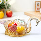 Glass swan-shaped bowl with fruits on a white surface, with apples and a yellow fruit in the foreground.
