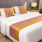 Bed with orange and yellow patterned pillows and bed runner in a modern bedroom.