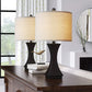 Two table lamps with beige shades on a wooden surface in a room with a window and decorative elements.