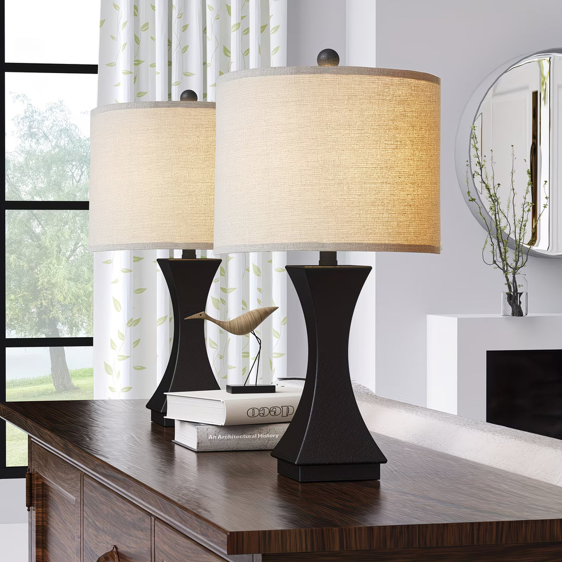 Two table lamps with beige shades on a wooden surface in a room with a window and decorative elements.