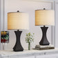 Two black table lamps with beige lampshades on a white surface, with a smartphone displaying charging symbols.