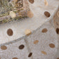 Close-up of a decorative fabric with gold thread and brown polka dots on a white background.