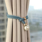 Curtain tieback with decorative beads on beige curtains against a blurred outdoor background