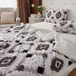 Bedroom with a bed covered in a patterned blanket and pillows, next to a nightstand with a lamp and decor items.