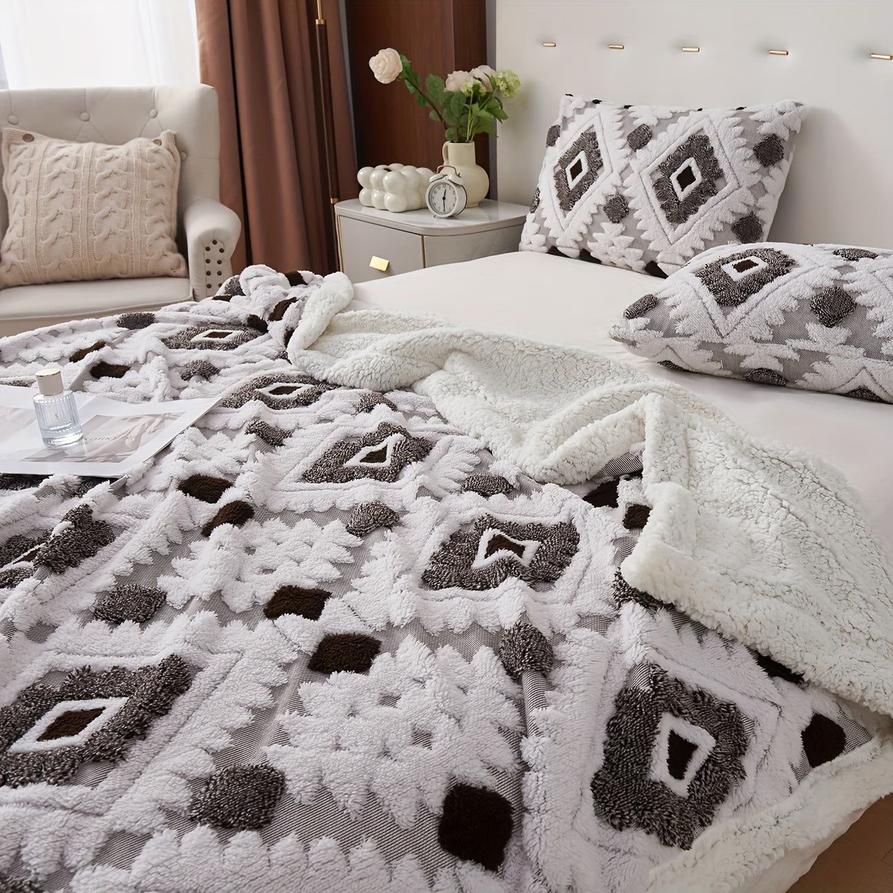 Bedroom with a bed covered in a patterned blanket and pillows, next to a nightstand with a lamp and decor items.