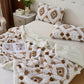 Patterned blanket and pillows on a bed with a side table in the background