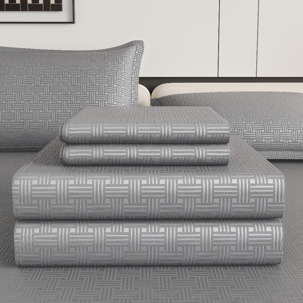 Stack of gray patterned bed sheets on a bed with pillows in a bedroom setting.