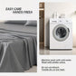 Gray bedding set on a bed with washing machine and laundry products in the background.
