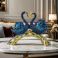 Decorative sculpture of two blue swans with a gold branch on a marble surface.