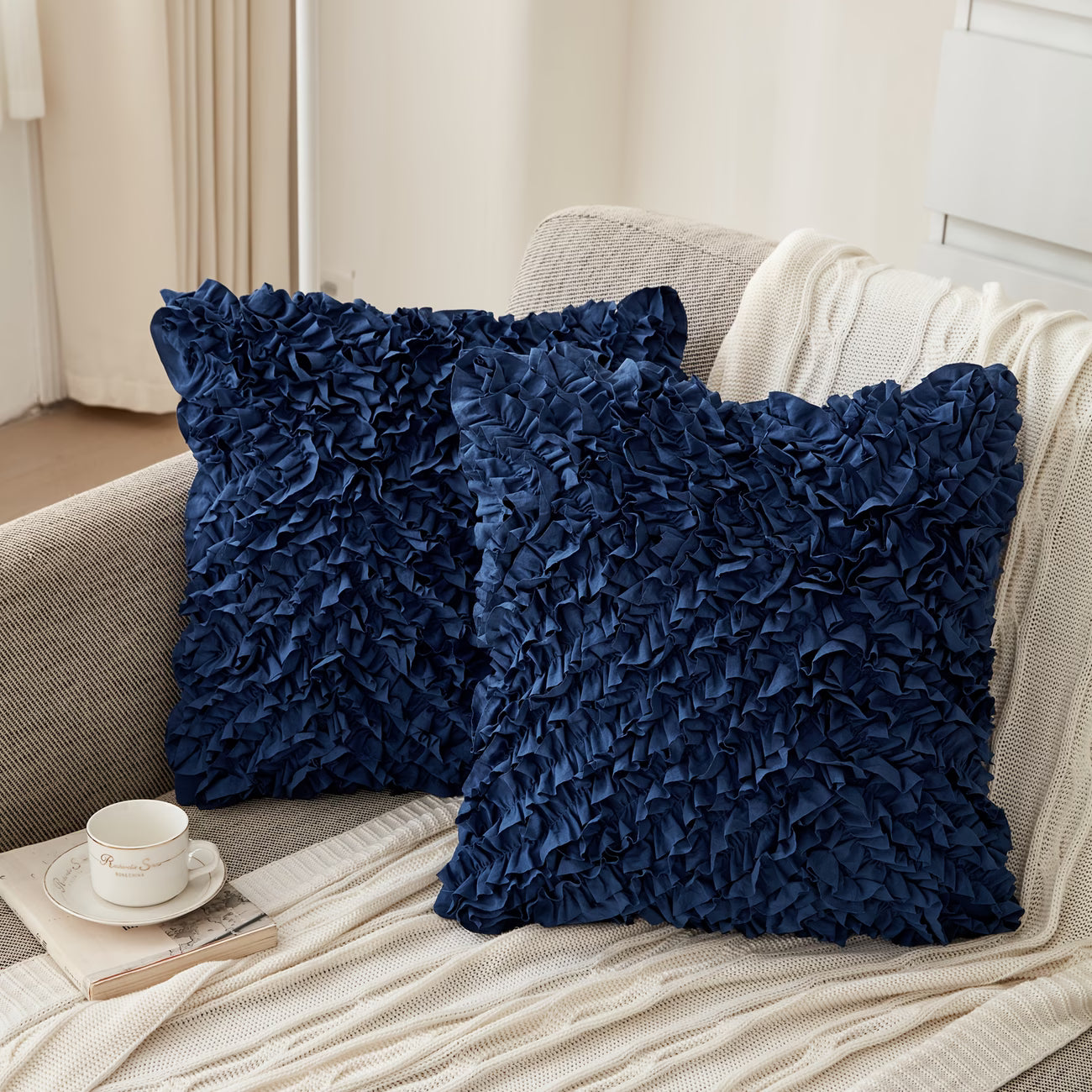 Two navy blue textured pillows on a beige sofa with a cup and saucer in the foreground.