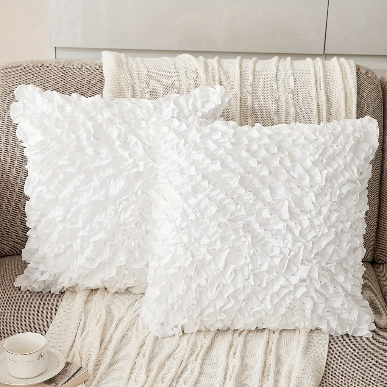 Two white textured pillows on a brown sofa with a cup and saucer in the foreground.