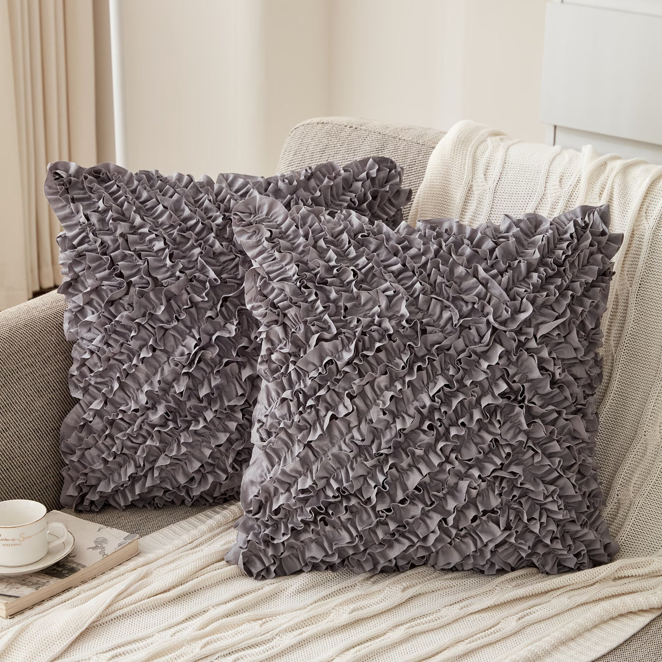 Two gray ruffled pillows on a beige sofa with a cup and saucer in the background.