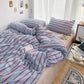 Bed with blue and red striped bedding in a room with a desk and lamp.