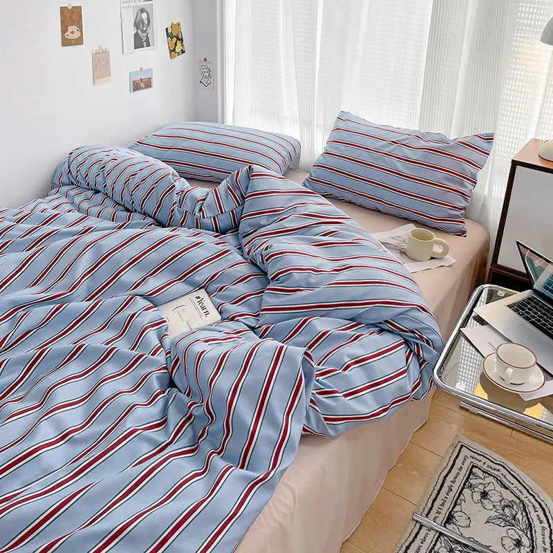 Bed with blue and red striped bedding in a room with a desk and lamp.