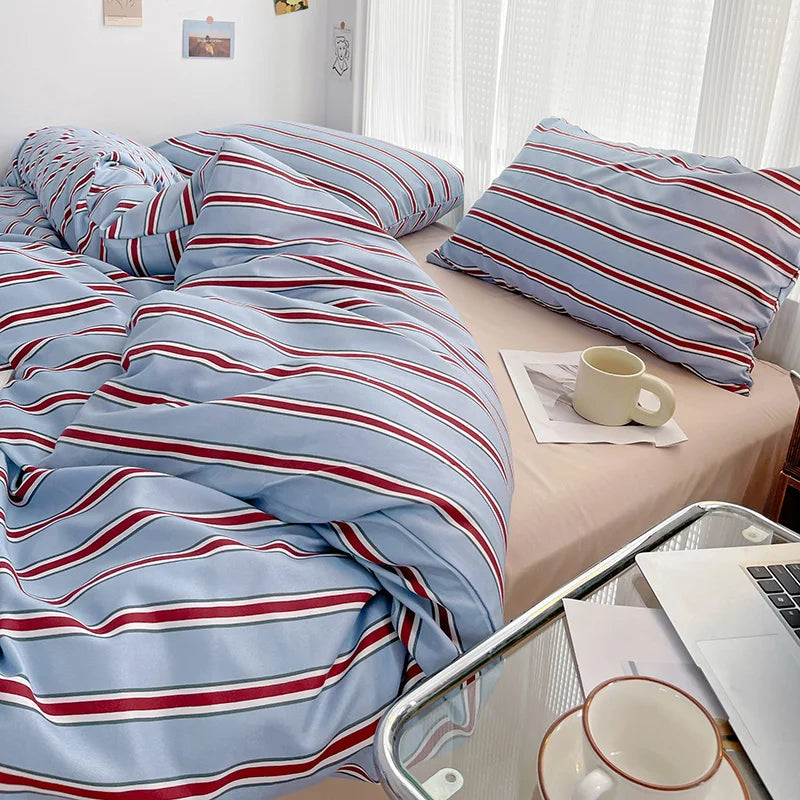 Bed with striped bedding and a cup on a nightstand, next to a laptop and tablet.