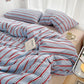 Striped bedding with red and blue lines on a bed in a bedroom setting.