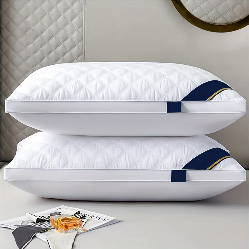 Two white pillows with blue and gold straps on a bed with a magazine and glass of water.