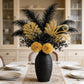 Decorative floral arrangement with black and gold feathers in a black vase on a table.