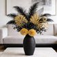 Decorative flower arrangement with black and gold flowers in a black vase on a table.