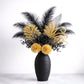 Decorative flower arrangement with black and gold flowers in a black vase on a white background