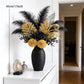 Decorative flower arrangement with black and gold flowers in a black vase on a white surface.