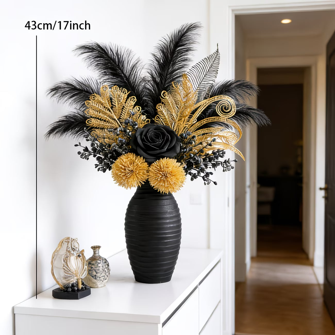 Decorative flower arrangement with black and gold flowers in a black vase on a white surface.