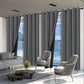 Modern living room with gray curtains, sofa, and chairs overlooking a scenic view.