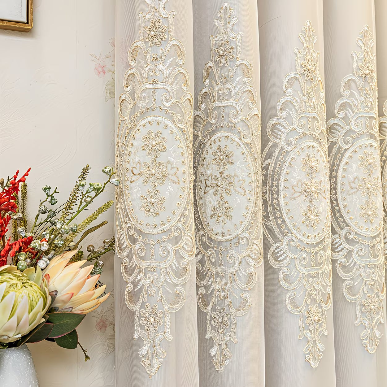 Decorative curtain with intricate gold embroidery next to a floral arrangement.