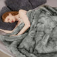 Woman lying under a fluffy gray blanket on a bed