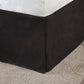 Black bedskirt corner on a bed with a textured gray carpet.