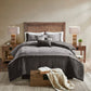 Bedroom with wooden bed frame, gray bedding, and nightstands with lamps.