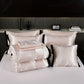Set of satin pillows and blankets on a bed with a dark headboard.
