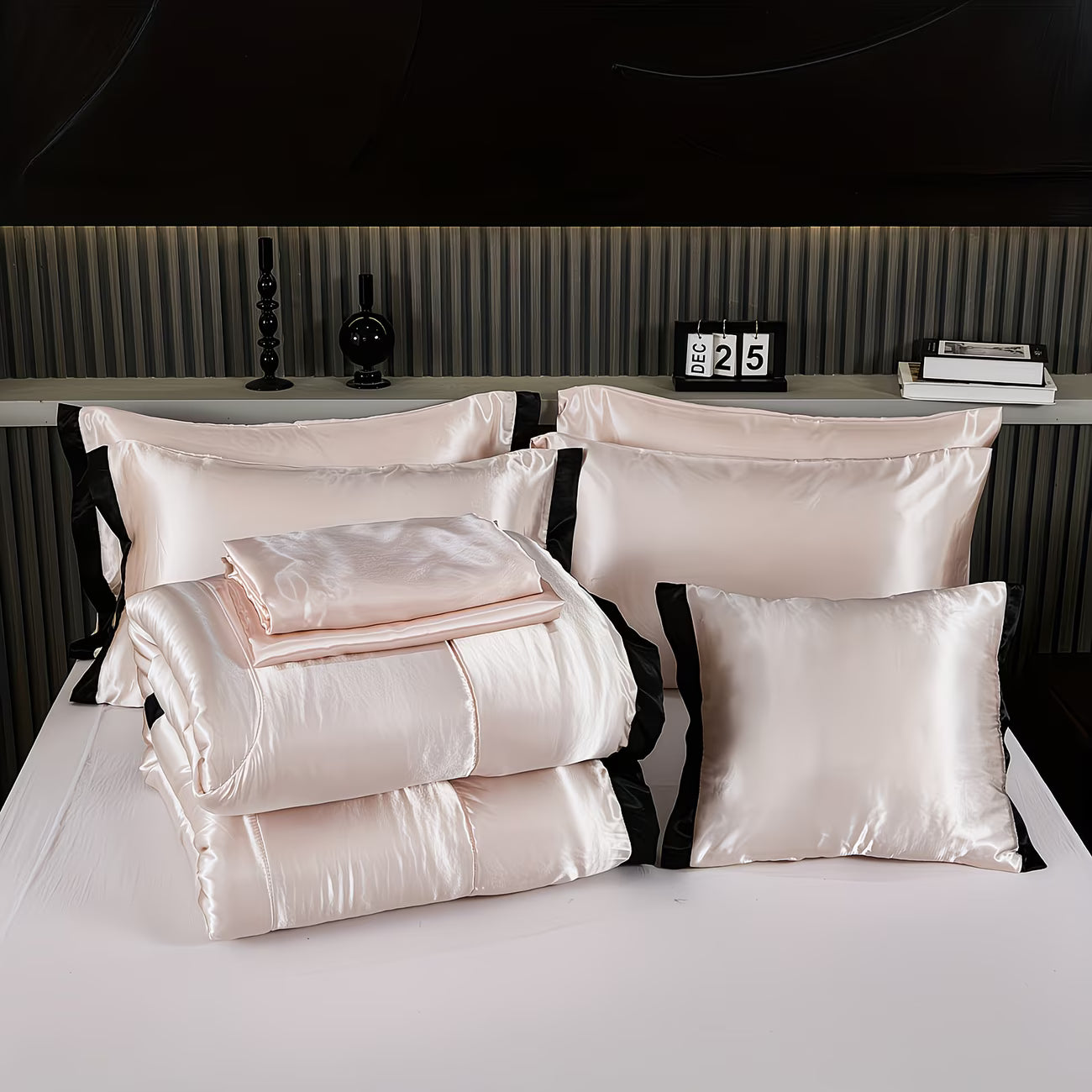 Set of satin pillows and blankets on a bed with a dark headboard.