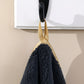 Black towel with gold trim hanging on a hook against a beige wall.