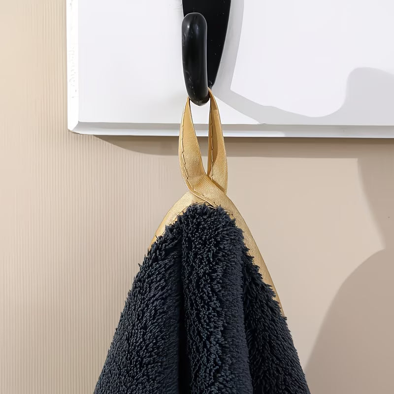 Black towel with gold trim hanging on a hook against a beige wall.