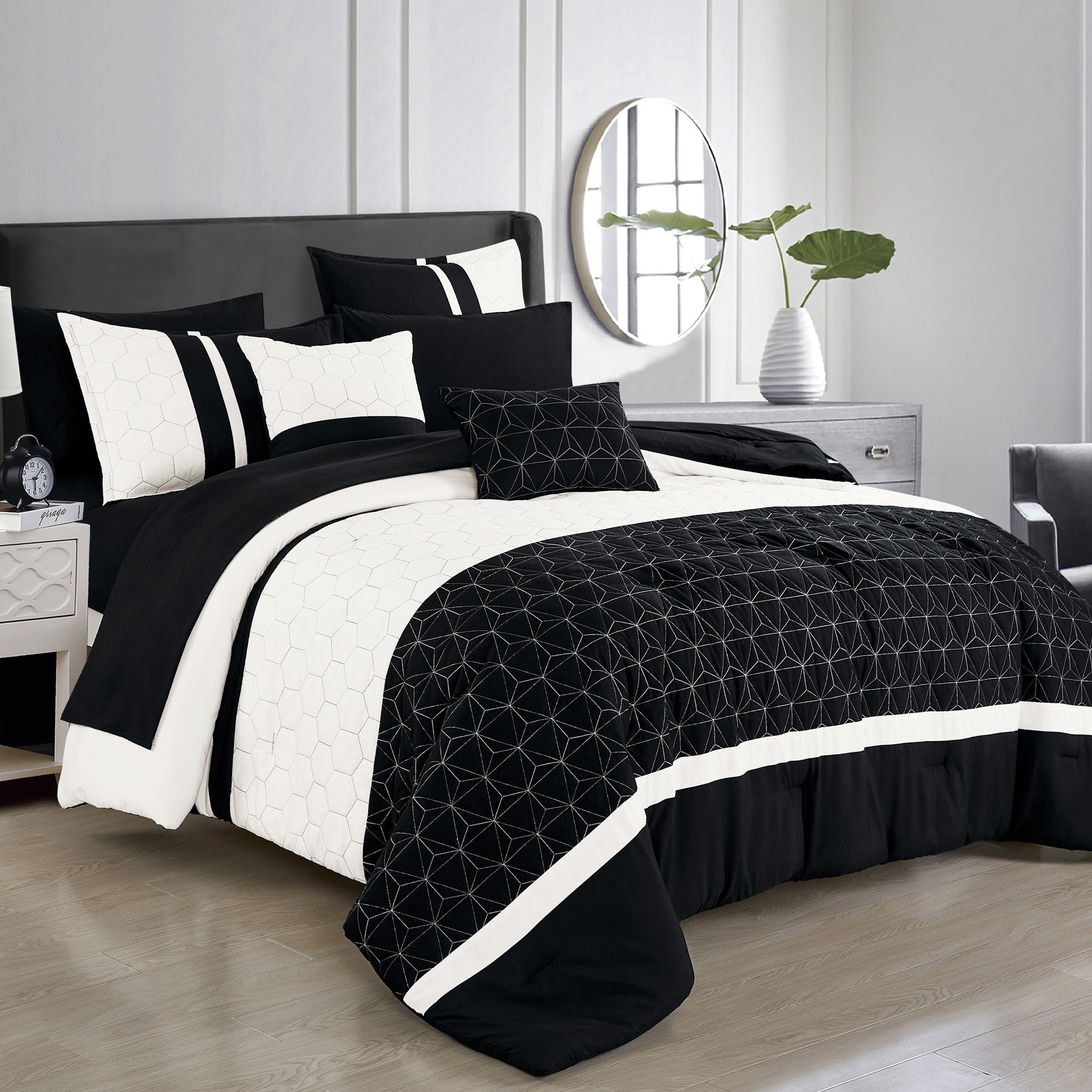 Black and white bedding set on a bed in a bedroom with a mirror and plant in the background.