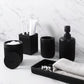 Black bathroom accessories including a soap dispenser, toothbrush holder, and towel on a marble countertop.